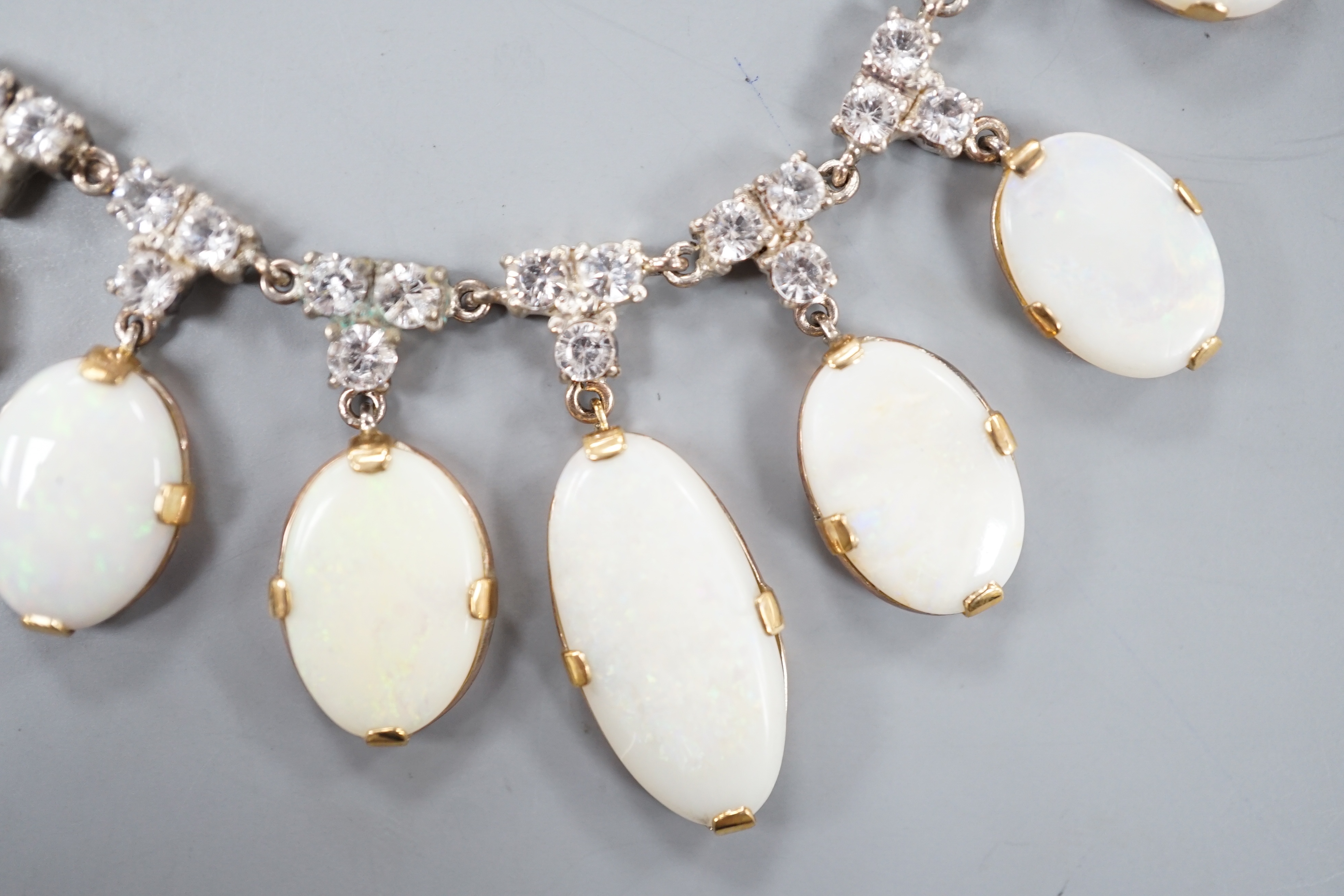 A yellow metal, graduated seven stone oval white opal and paste set cluster fringe necklace, 42cm, gross 14.6 grams.